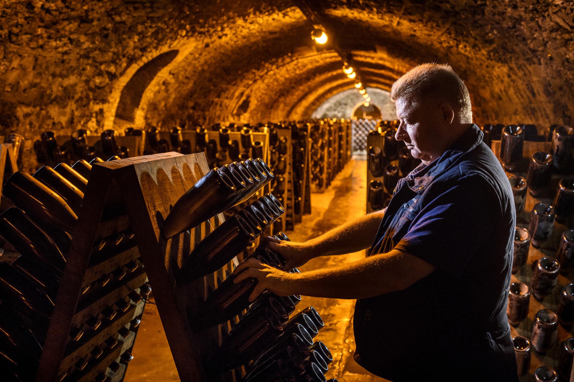 Kellermeister rüttelt Champagnerflaschen im Rüttelpult in einem Gewölbekeller